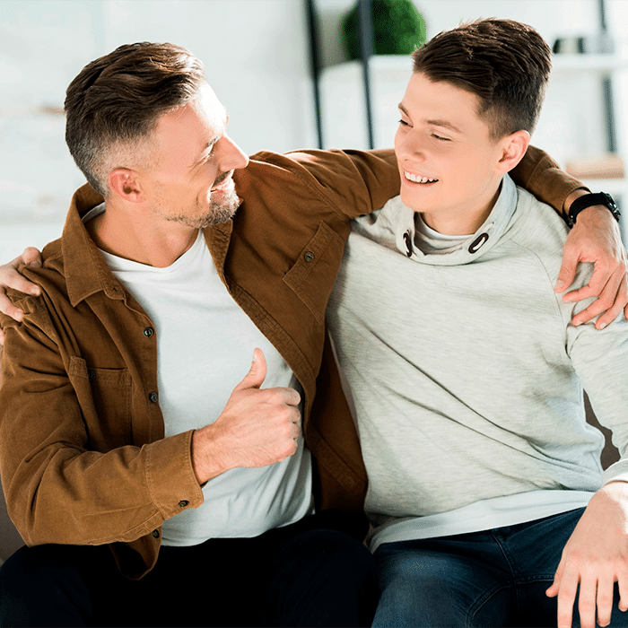 smiling-father-and-teen-son-hugging-on-sofa-at-hom-2022-12-16-21-09-08-utc@2x